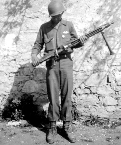 Homer F. Petross holding a German burp gun in front of a stone wall.jpg
